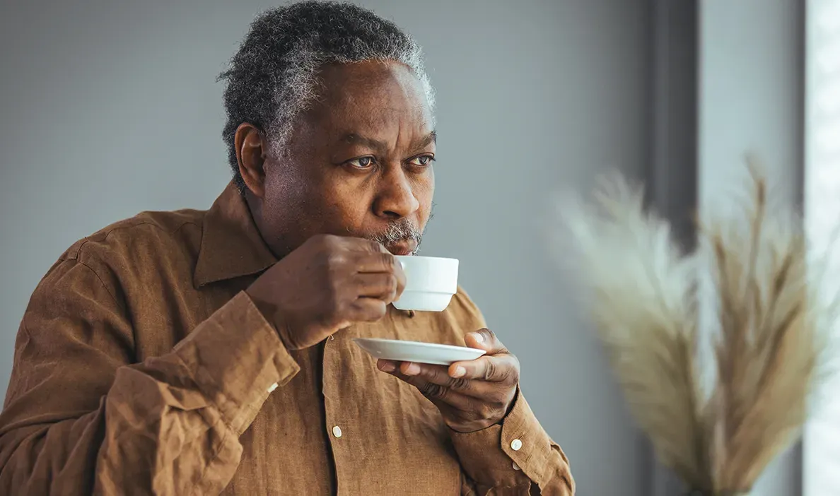man with graying hair sipping from a white teacup, appearing to be in a moment of contemplation.