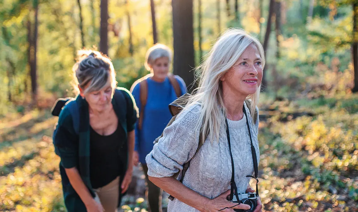 Group of women hiking in the forest, smiling and enjoying the fresh air while carrying backpacks.