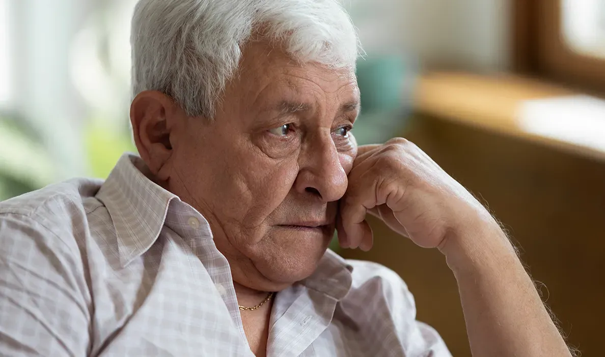 Man with white hair resting his head on his hand, appearing pensive as he looks off into the distance.